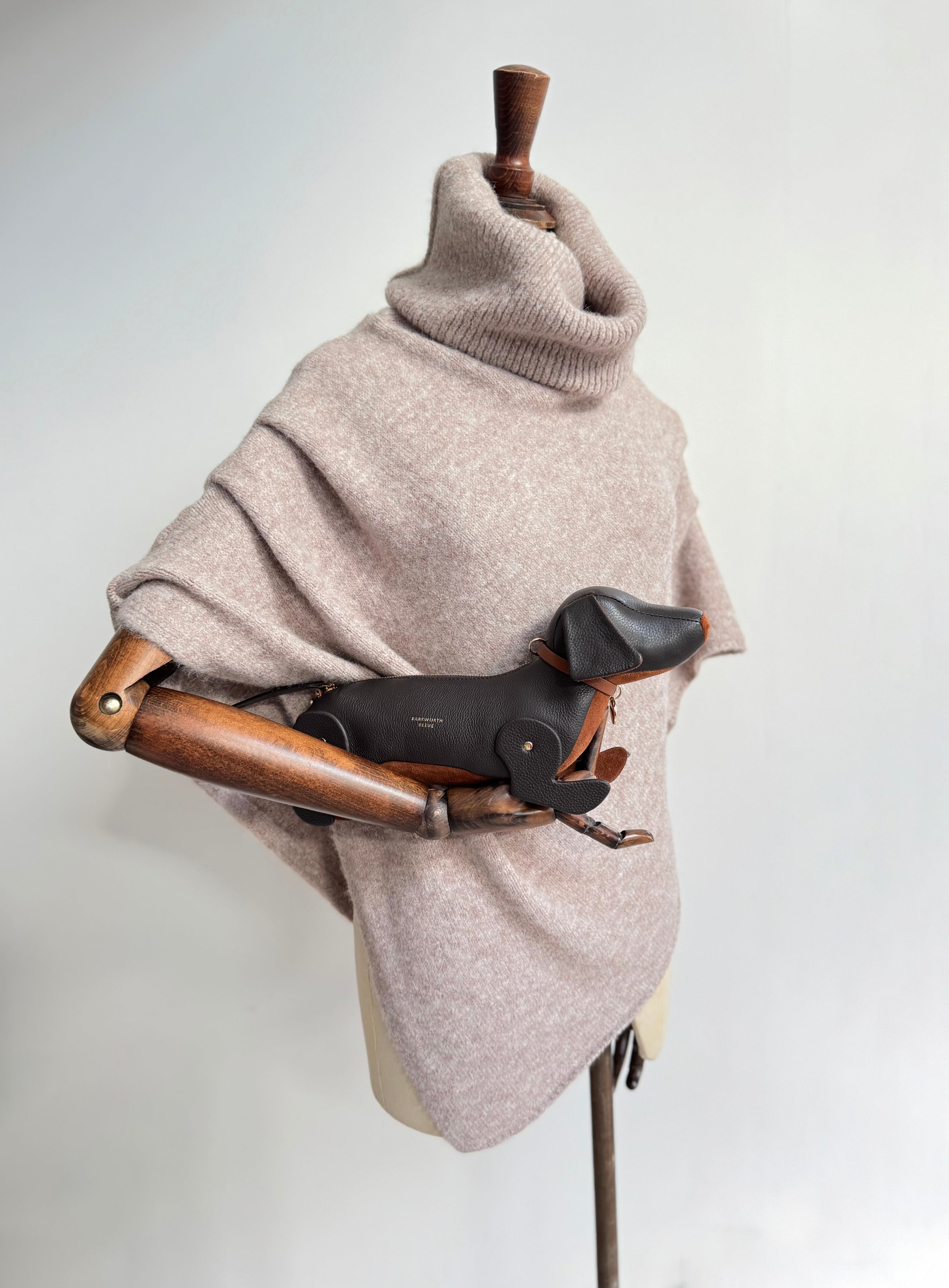 Sausage dog bag with chcolate leather exterior and tan suede tummy. Carried as a clutch bag. mannequin is wearing a knitted poncho with a large roll neck