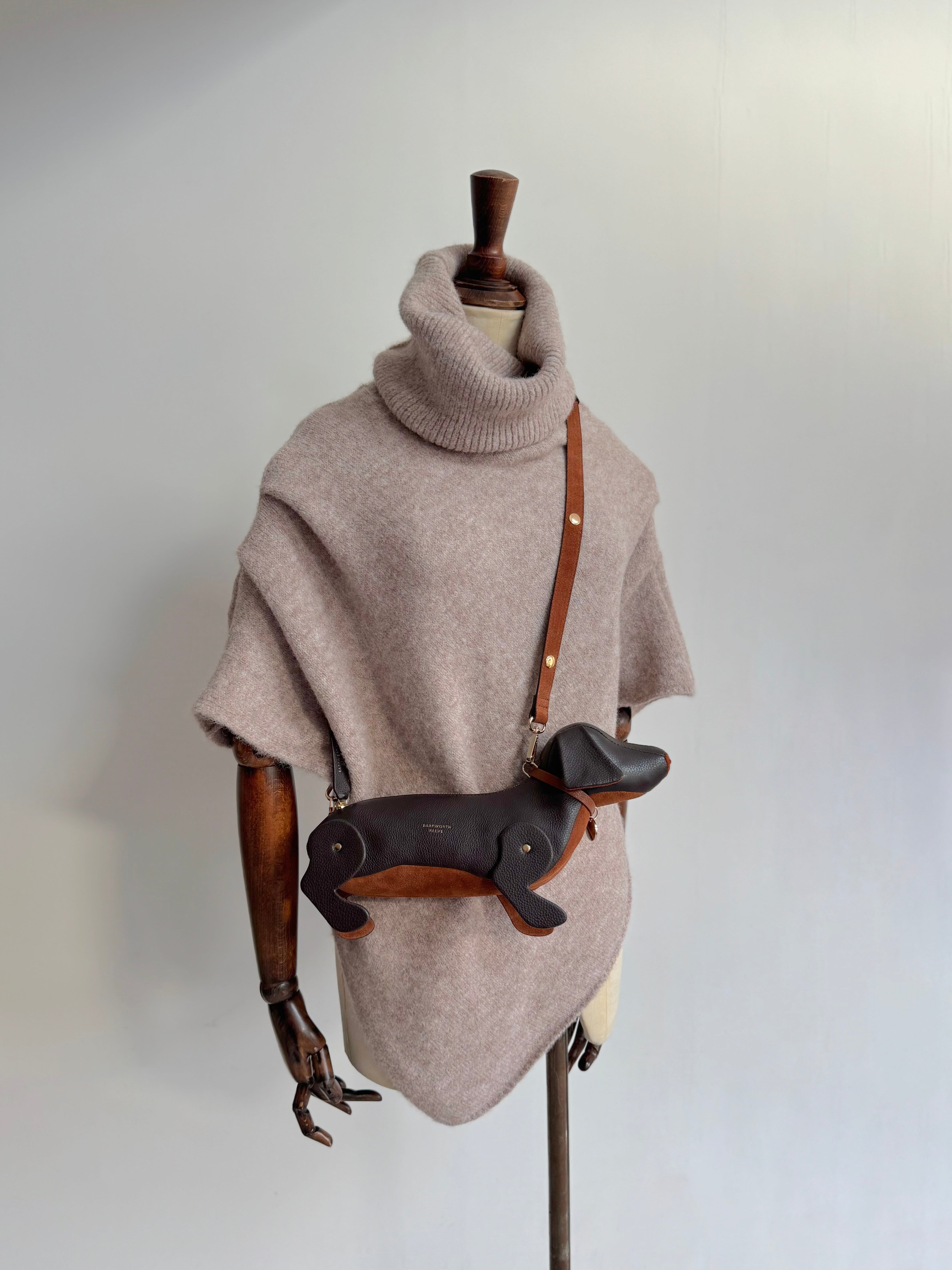 Sausage dog bag with chcolate leather exterior and tan suede tummy. Worn as a cross body bag. mannequin is wearing a knitted poncho with a large roll neck