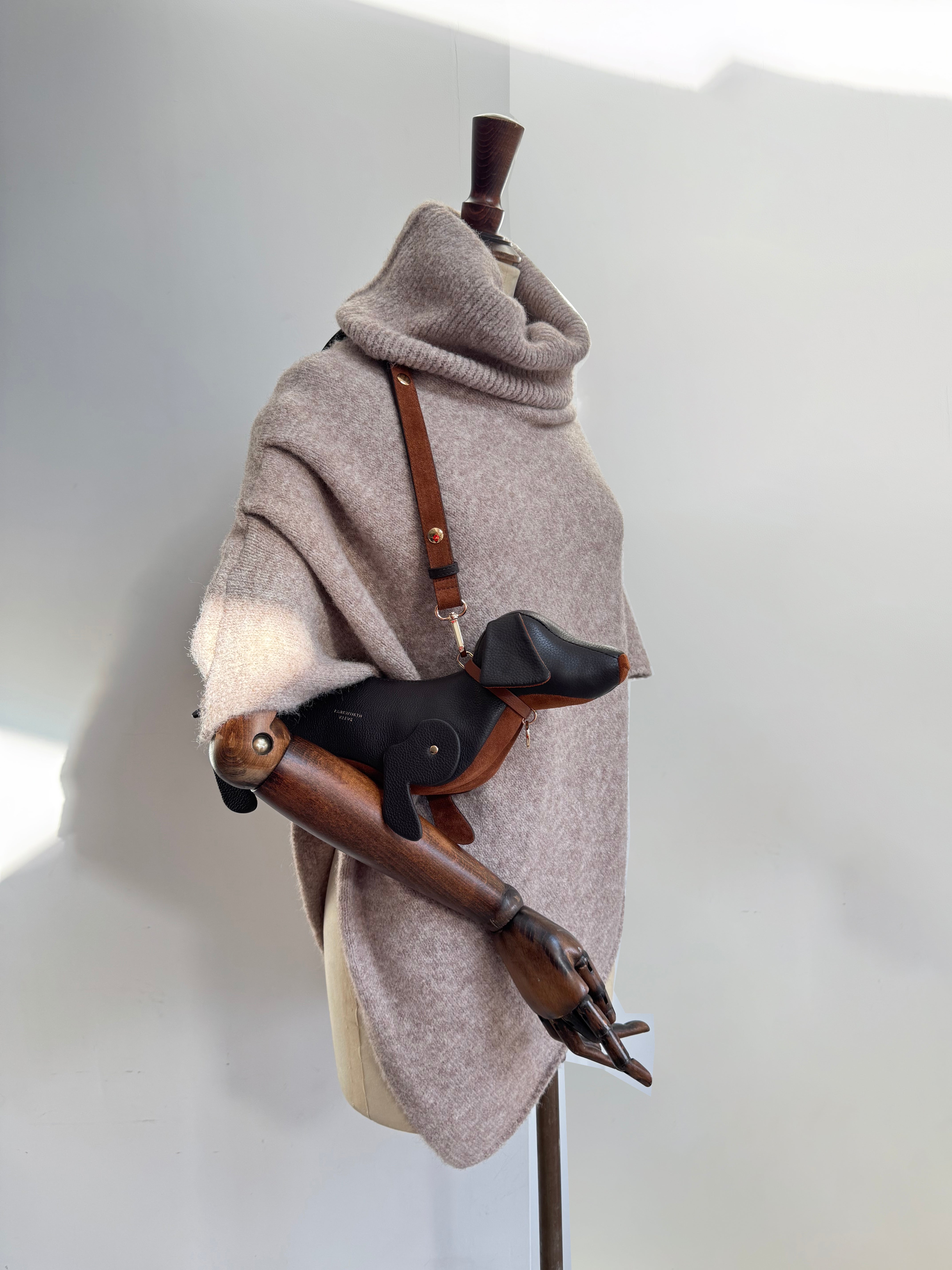 Sausage dog bag with chcolate leather exterior and tan suede tummy. Carried as a shoulder bag. mannequin is wearing a knitted poncho with a large roll neck