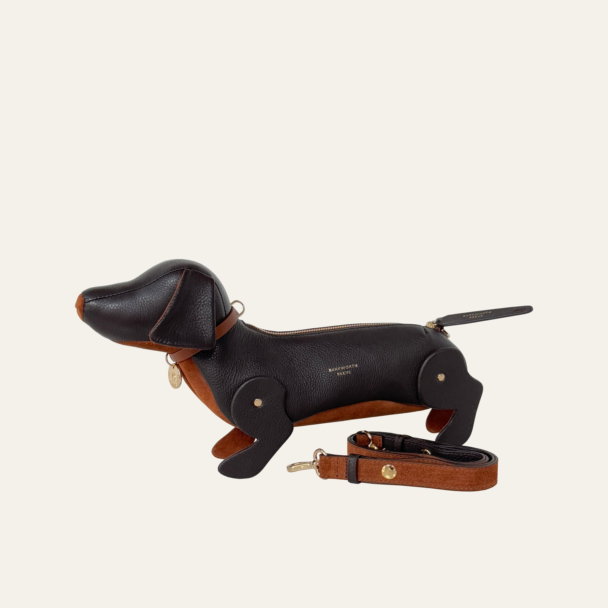 Leather sasuage dog handbag with adjustable shoulder strap laying next to the bag. handbag is chocolate brown leather with a tan suede tummy and a brass zip opening on the back of the dog.
