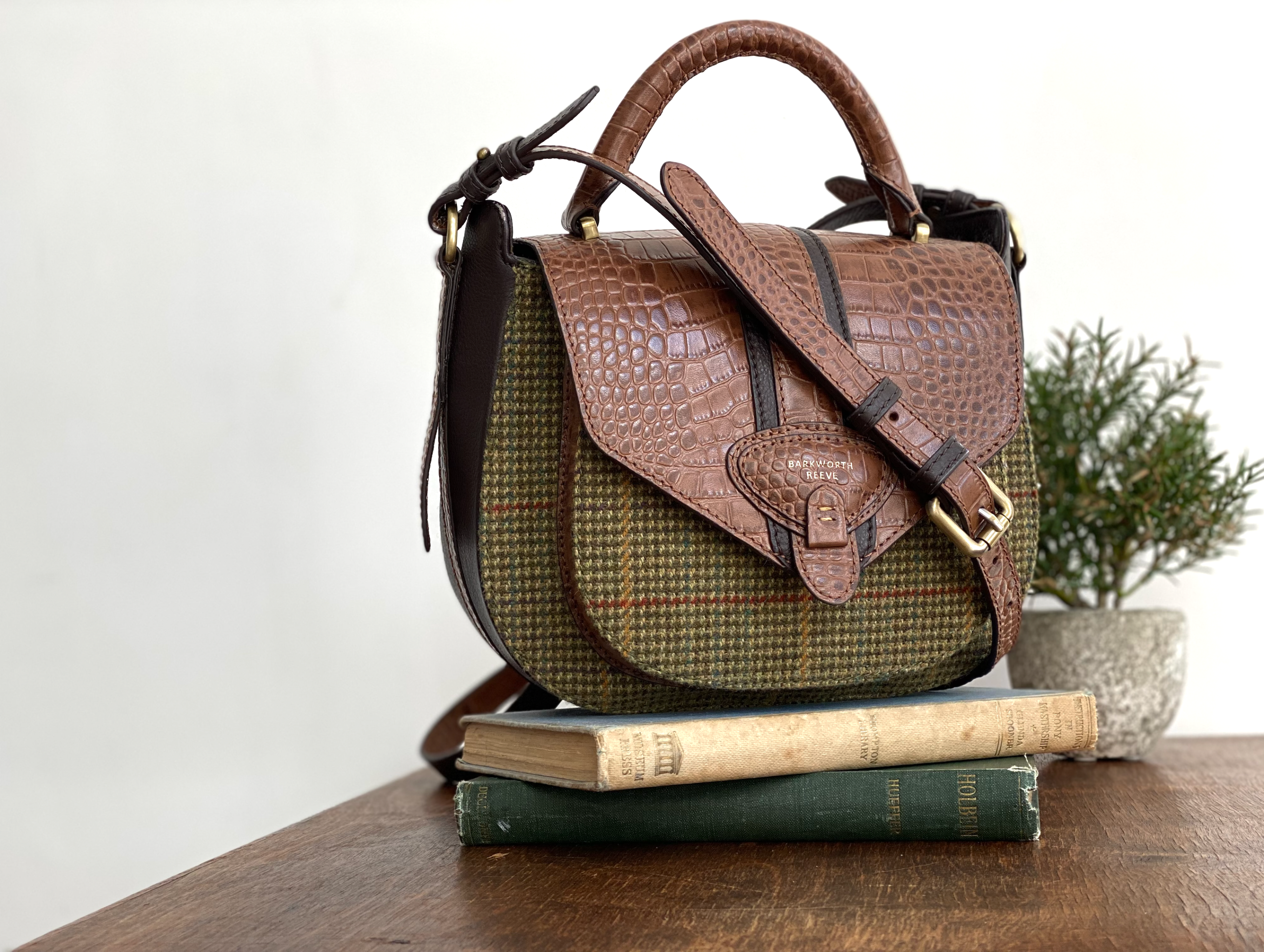 Tweed and embossed croc leather Belton saddle bag by Barkworth Reeve on a stack of books