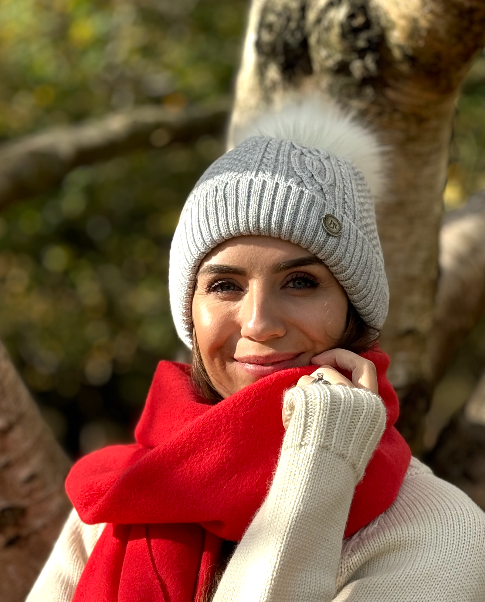 lady smiling wearing grey bobble hat with red scarf in an autumn wood