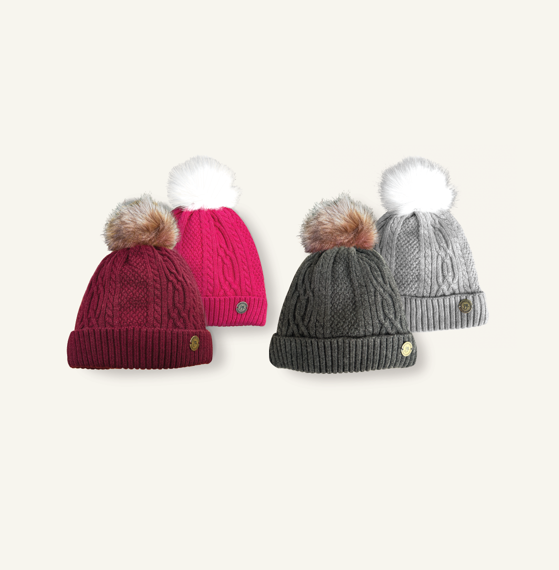 raspberry pink bobble hat with white faux fur pom pom, dark red bobble hat with natural coloured pom, light grey bobble hat with white pom, and dark grey hat with natural coloured pom, all knitted in a mixed cable knit pattern with branded barkworth reeve tab