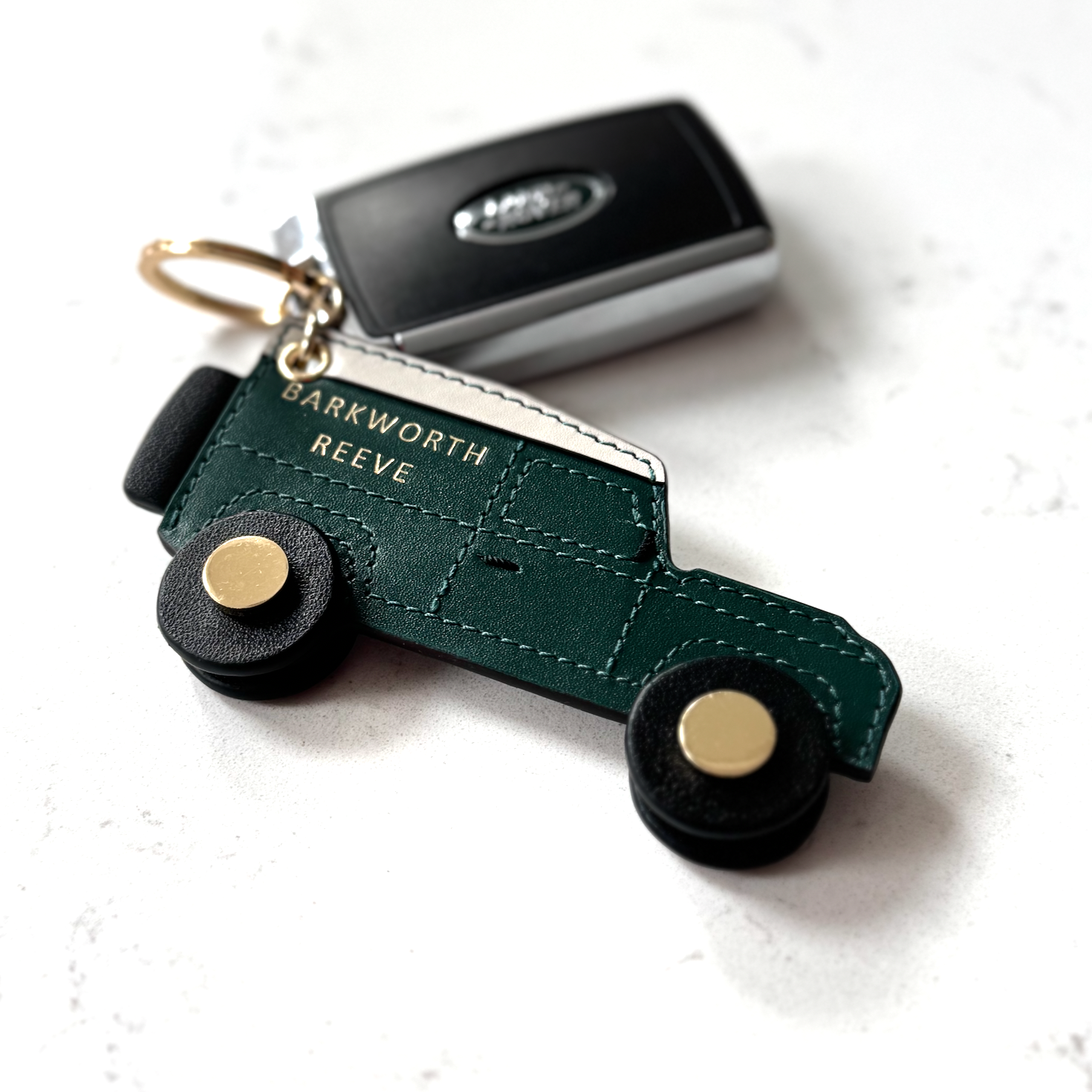Green leather 4x4 off road keyring with black rotating wheels and keys on marble worktop