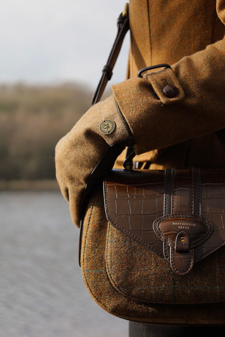 TWEED AND CROC LEATHER SADDLE BAG, ZOOMED IN ON A WOMAN SHOULDER INFRONT OF A LAKE