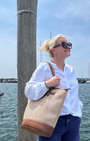Woman holding a woven bag by a dock with water and sky in the background