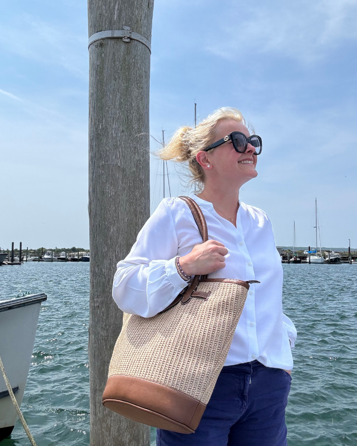 Woman holding a woven bag by a dock with water and sky in the background