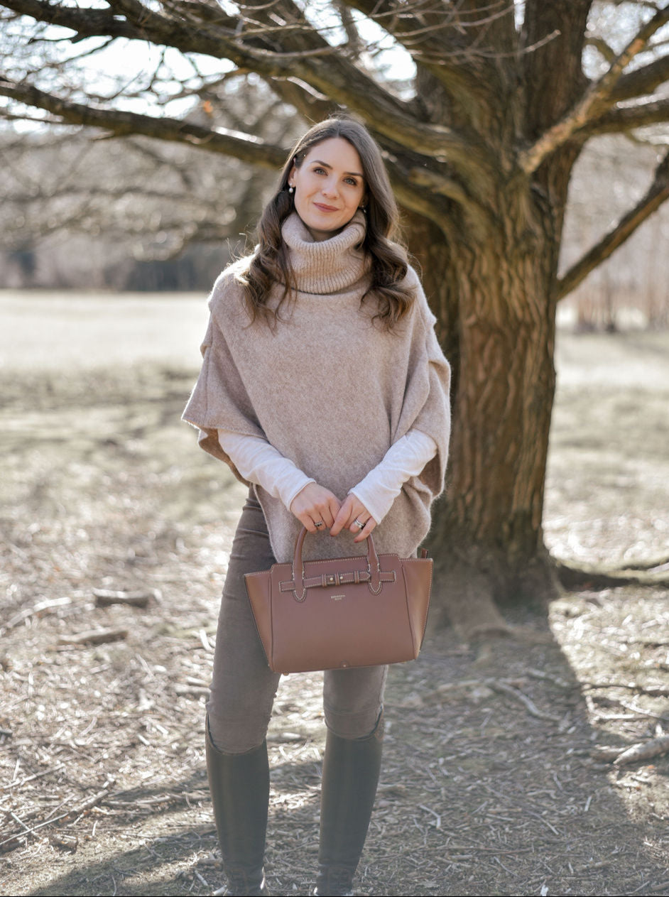 woman stood in front of tree wearing a knitted realed oat coloured poncho with a brown leather Middelton Bag from Barkworth Reeve