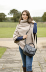 Woman wearing a beige poncho and blue jeans, holding a gray handbag in an outdoor setting.