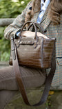 CHOCOLATE CROC LEATHER HANDBAG ON A WOMANS LAP. WOMAN WEARING A TWEED JACKET