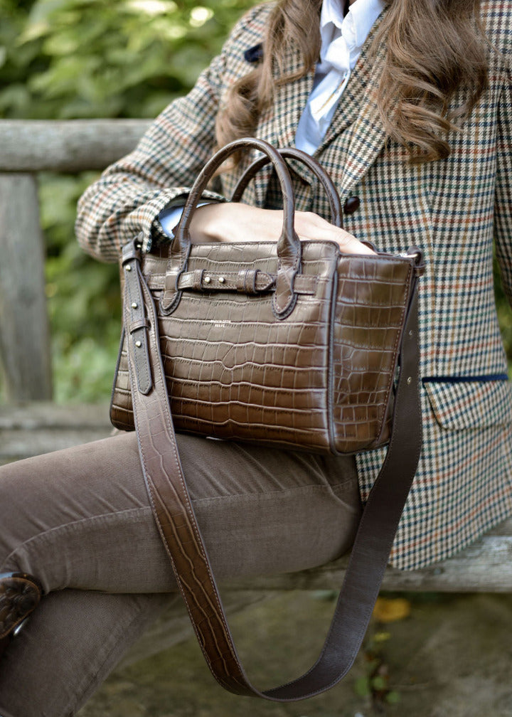 CHOCOLATE CROC LEATHER HANDBAG ON A WOMANS LAP. WOMAN WEARING A TWEED JACKET