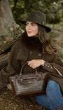 WOMAN IN WAXED HAT AND CROC LEATHER HANDBAG SAT UNDER A TREE