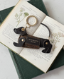 chocolate leather sausage dog keyring wearing a tweed coat with a gold hoop attachment laid on a book 