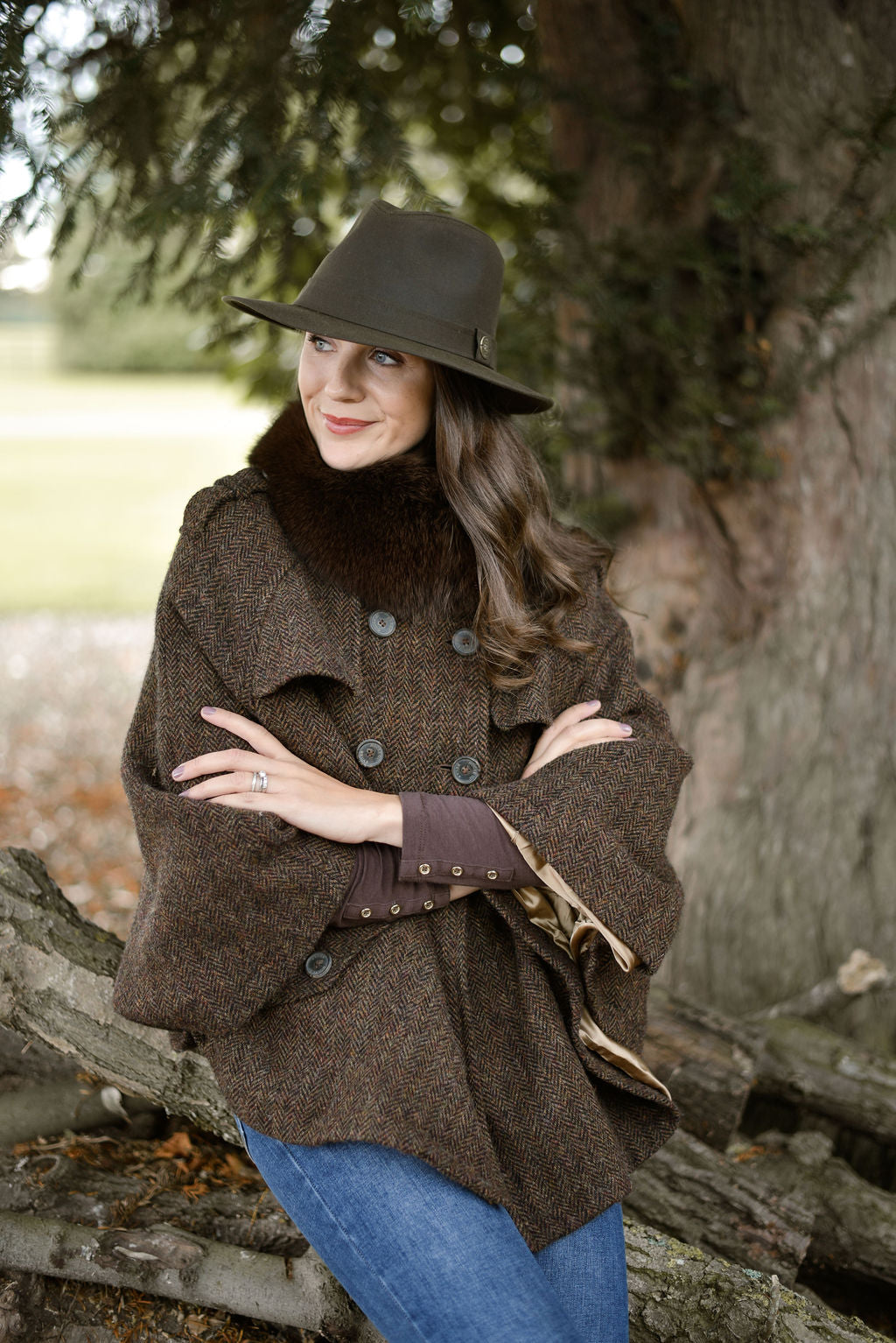 Woman wearing a brown coat and hat standing outdoors near a tree