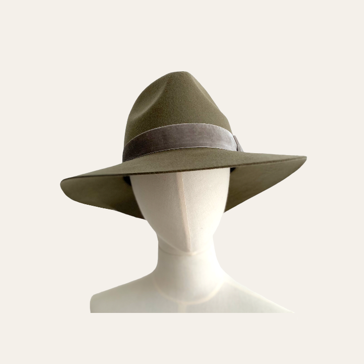 A wide brimmed fedora hat in soft olive green, displayed on a mannequin head.