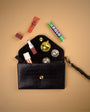 navy blue leather clutch bag open with makeup items spilling out on a beige background