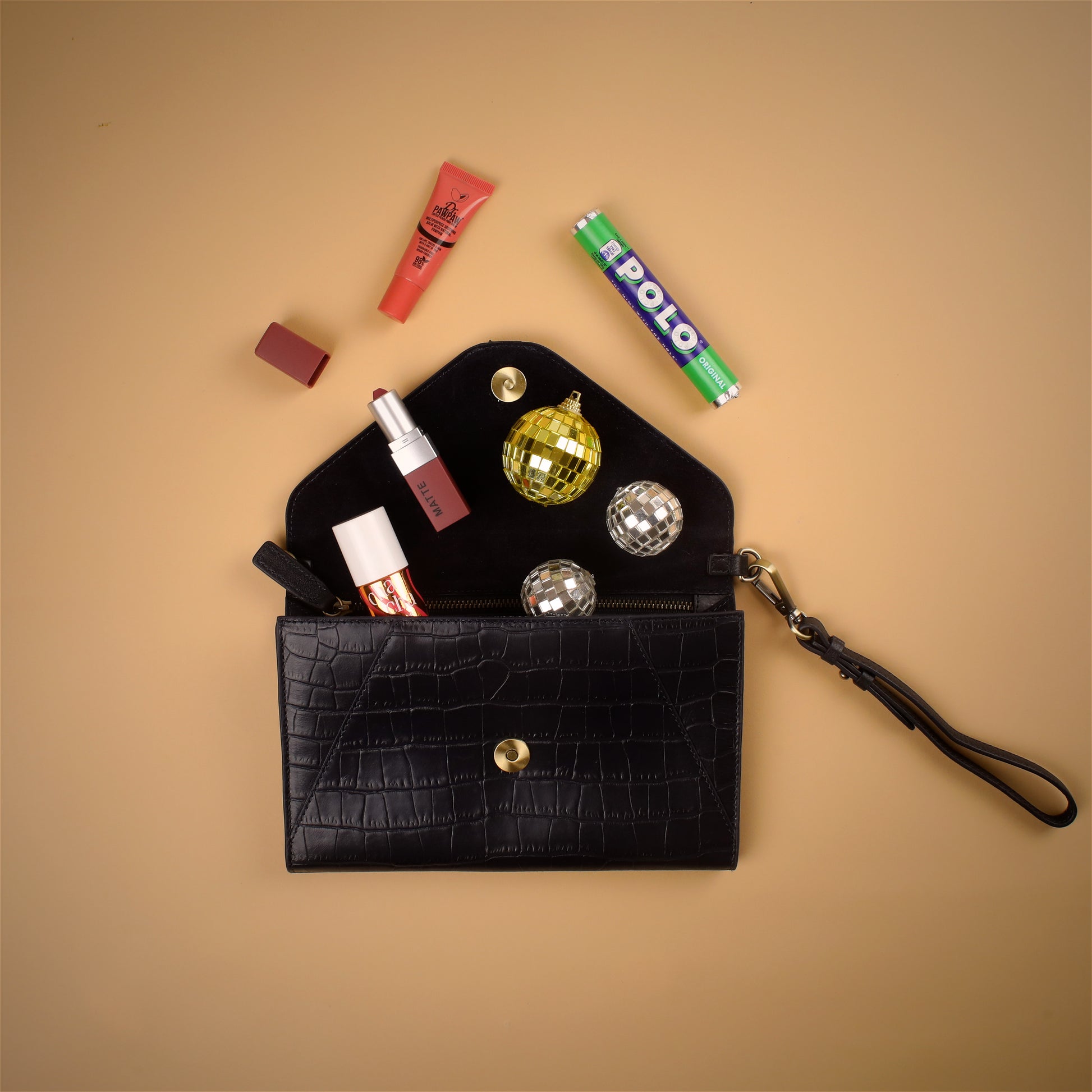 navy blue leather clutch bag open with makeup items spilling out on a beige background