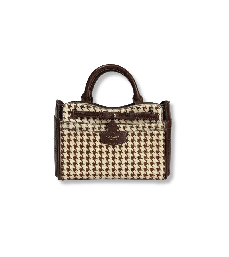 A structured handbag with a brown and beige houndstooth pattern, dark brown leather trim, a top handle, and a central hanging strap detail, shown against a plain white background.