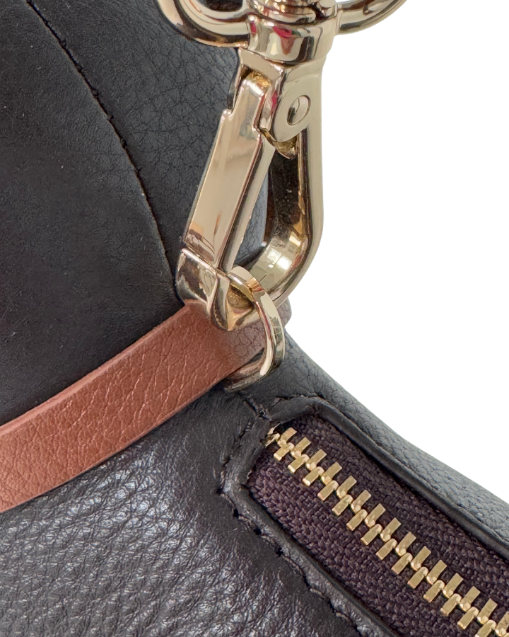 Close-up of a black leather wallet with gold zipper pull and brown strap.