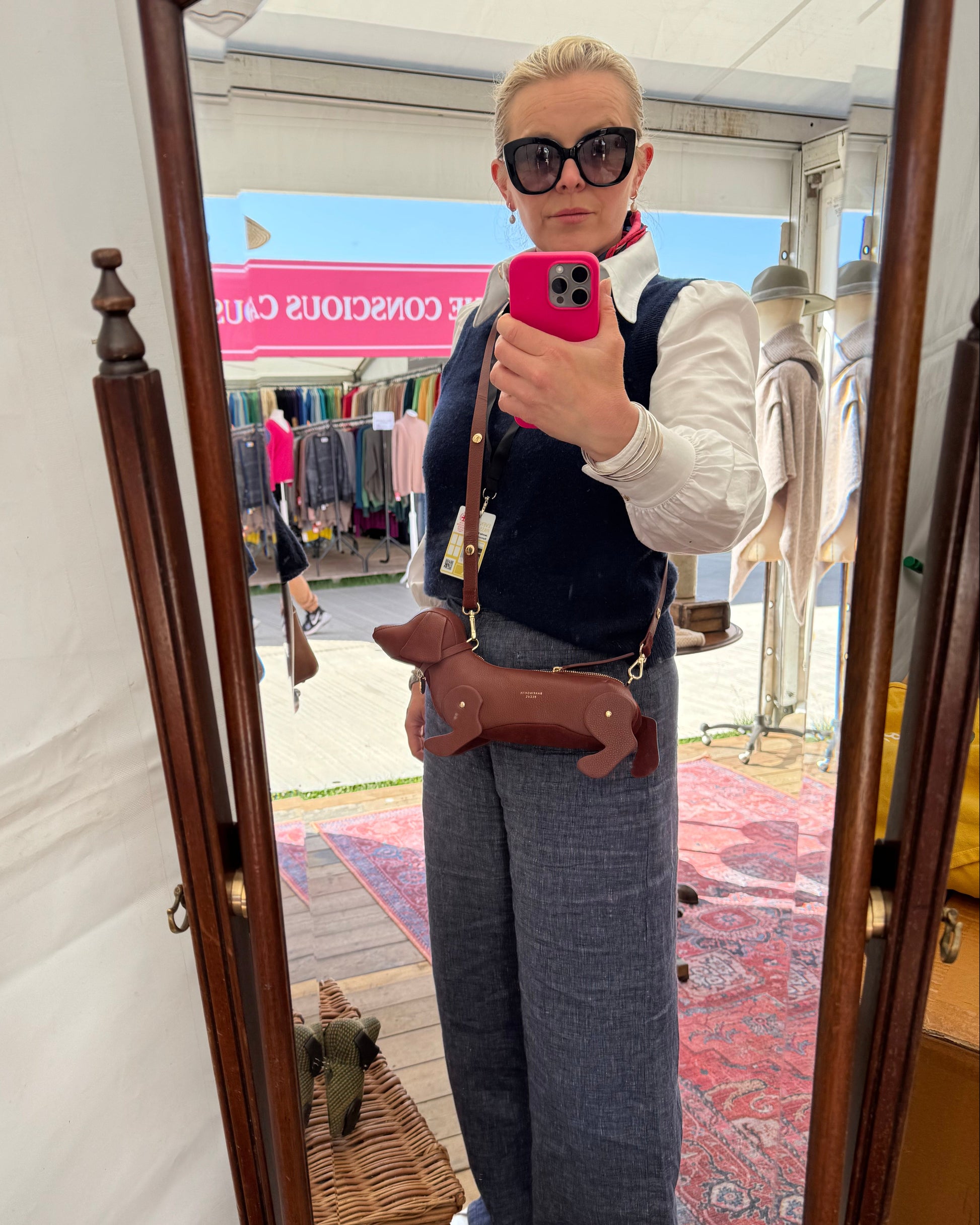 Person taking a mirror selfie wearing sunglasses and a white shirt with a patterned background.