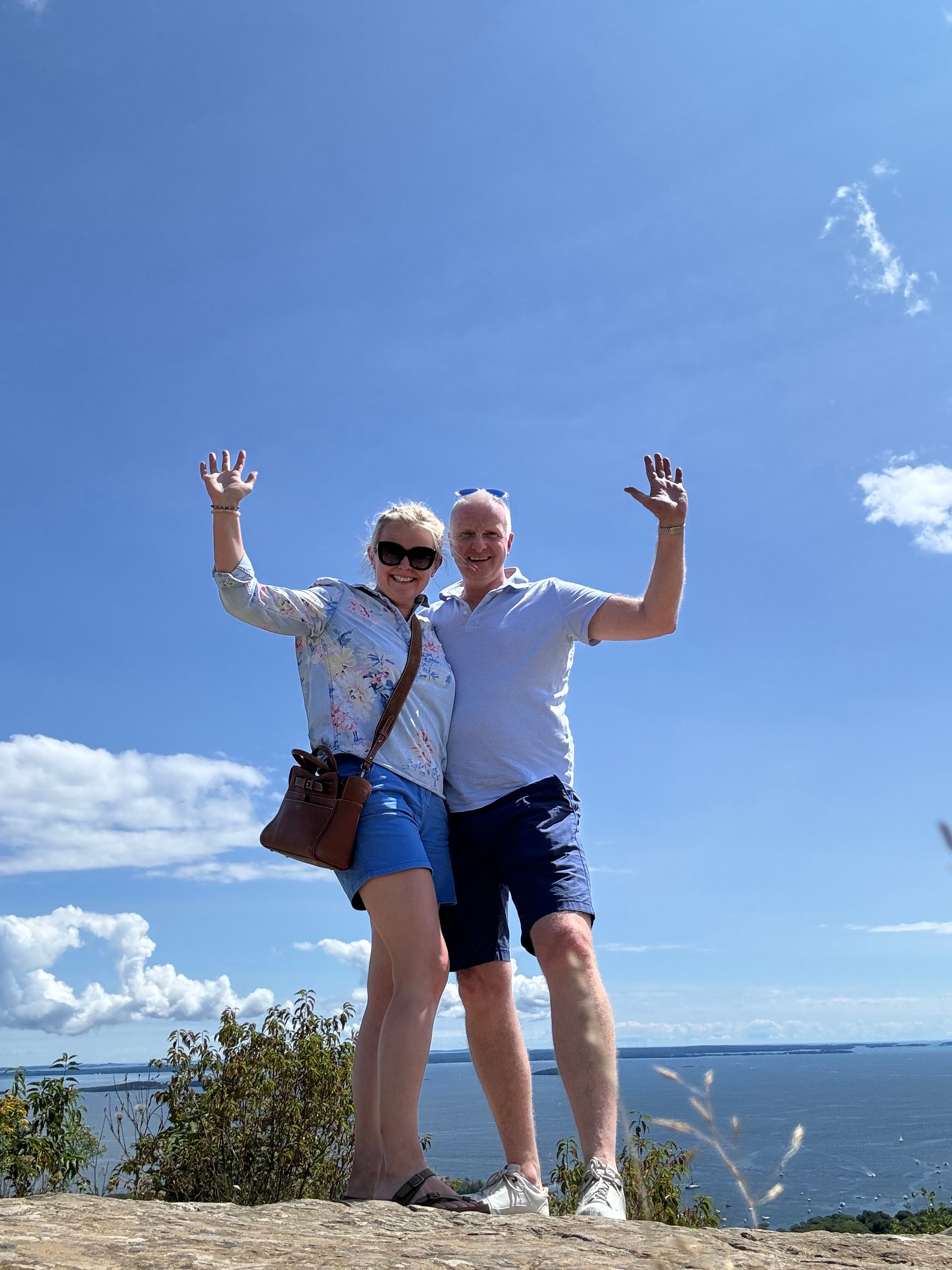Two people posing for a photo with a scenic background of trees and blue sky.