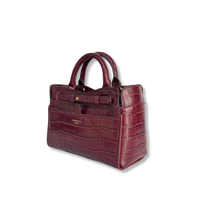 A structured handbag in embossed crocodile-look leather in a deep burgundy red, featuring dual top handles, a front flap pocket, and gold-tone hardware. The brand name 'PETERSEN PARIS' is visible in gold lettering on the front.