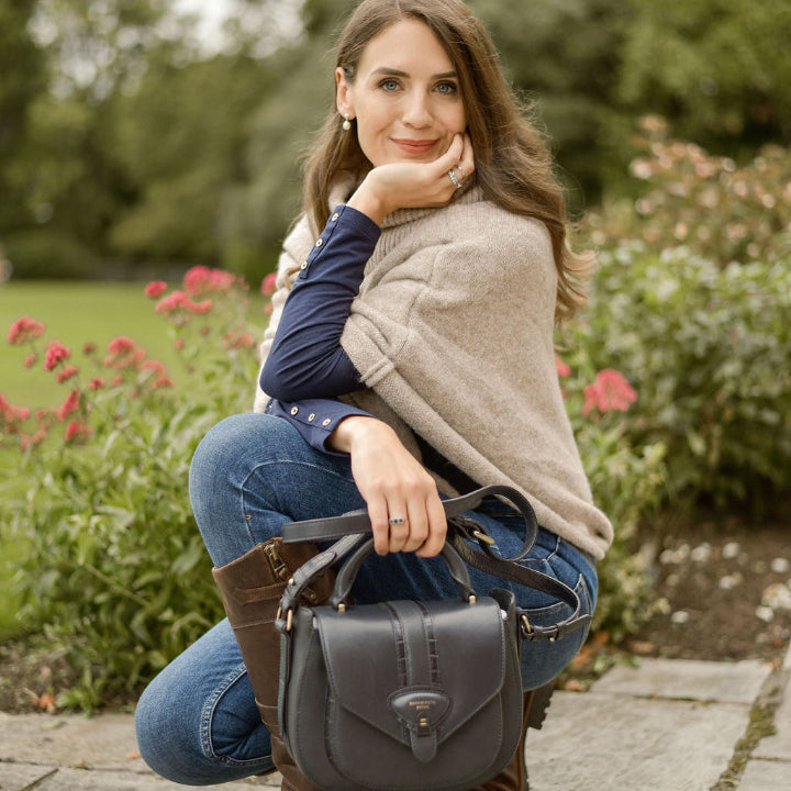 woman kneeling down on patio wearing jeans and boots, hlding a navy leather bag 