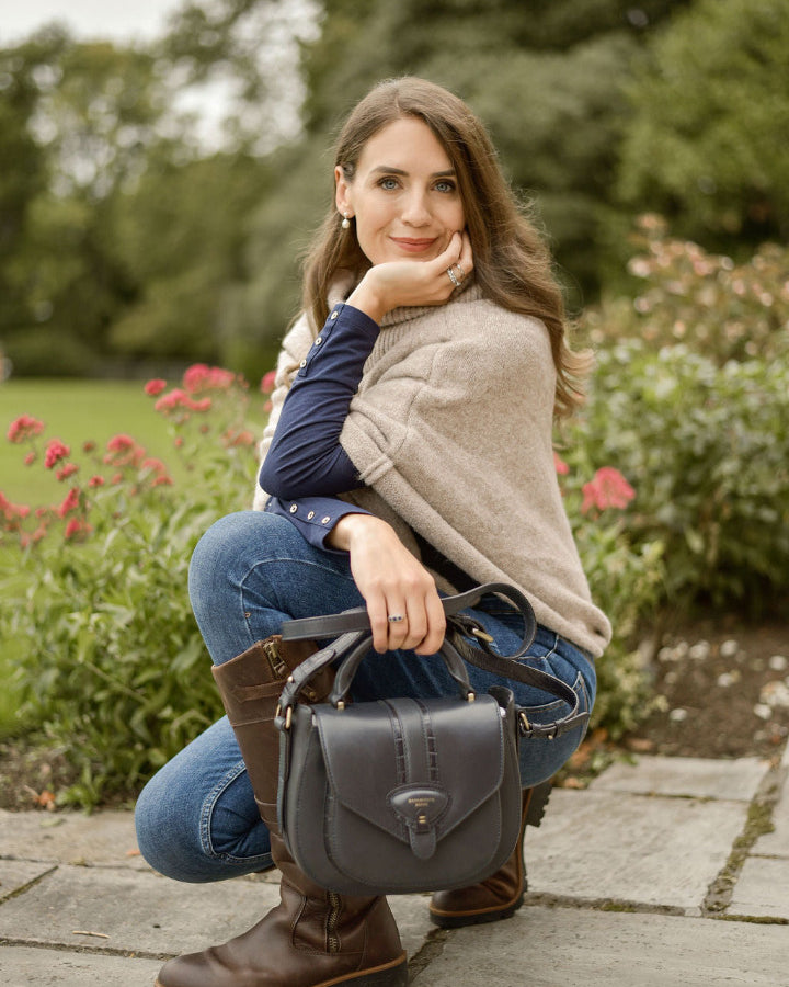 woman kneeling down on patio wearing jeans and boots, hlding a navy leather bag 