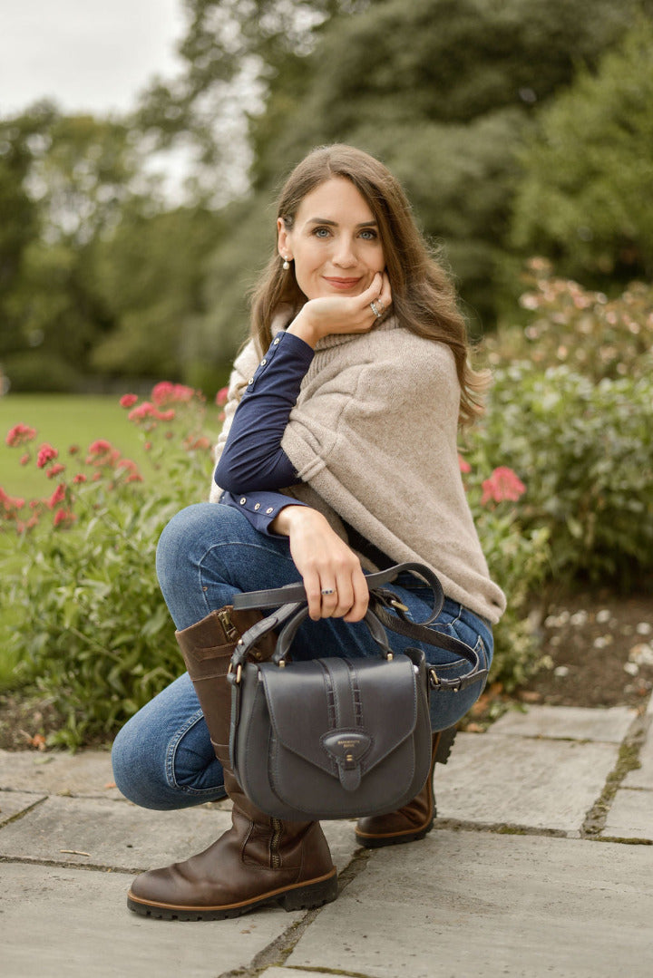 woman kneeling down on patio wearing jeans and boots, hlding a navy leather bag 