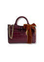 A burgundy crocodile-embossed leather handbag with a top handle, gold chain strap, and a large rust-brown velvet bow on the front, shown on a plain white background.