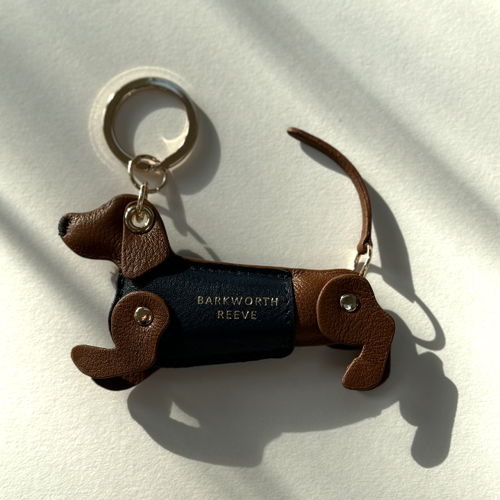 tan leather dachshund keyring, with blue leather coat and gold keyring split ring on a shadow background