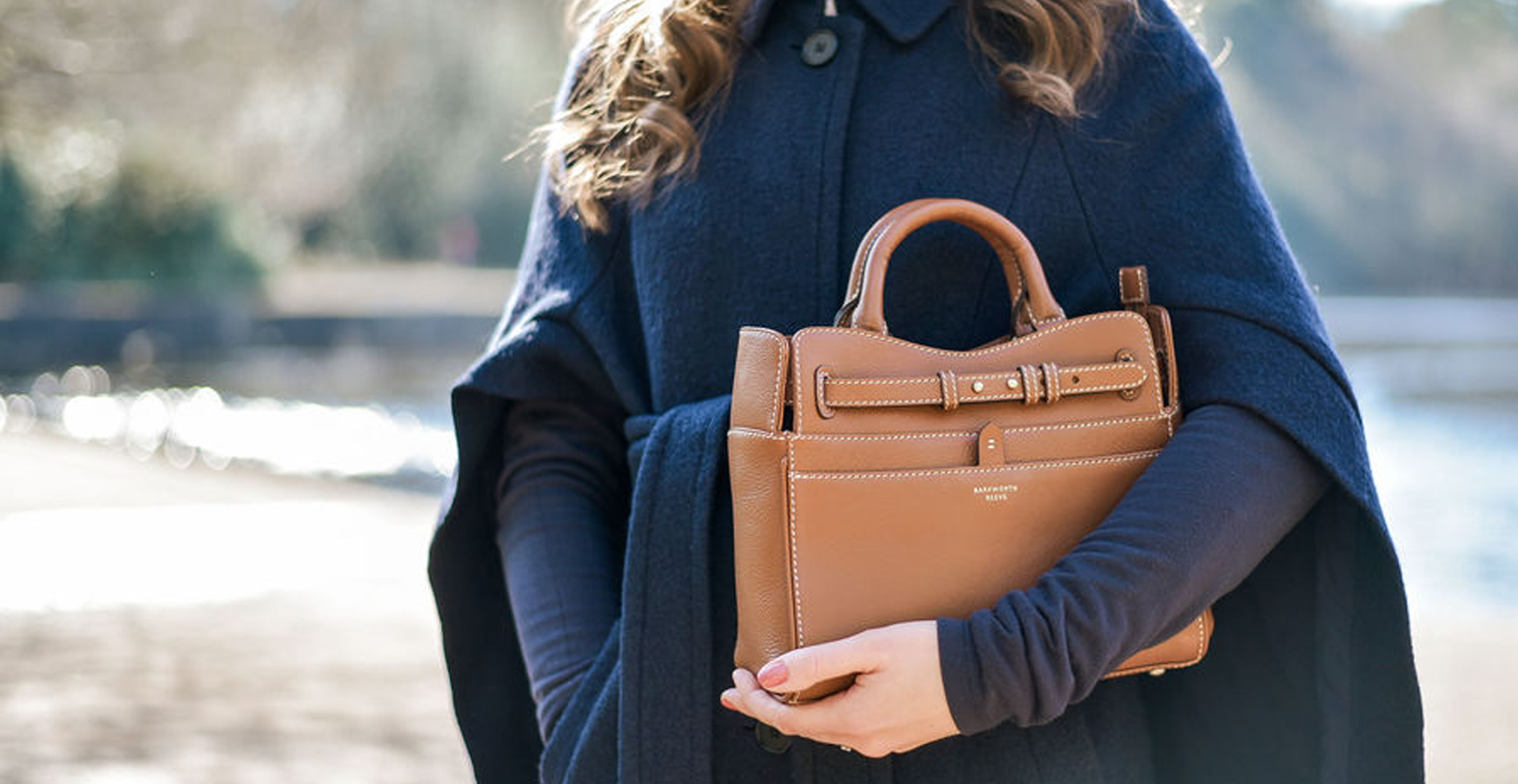 Woman holding a Tan Leather Ambridge hand held bag by Barkworth Reeve in country setting