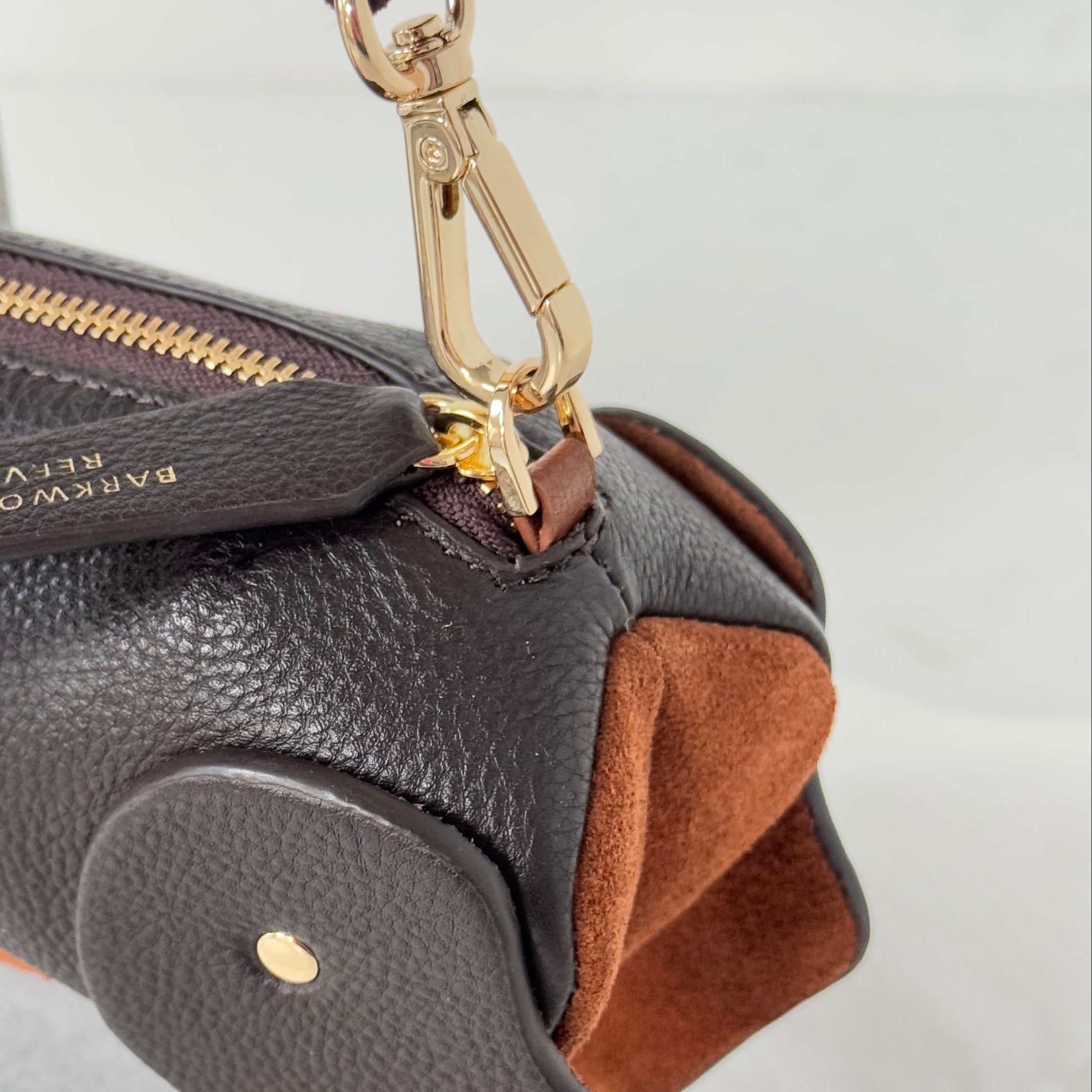 Close-up of a black leather handbag with brown interior and gold zipper on a light gray background