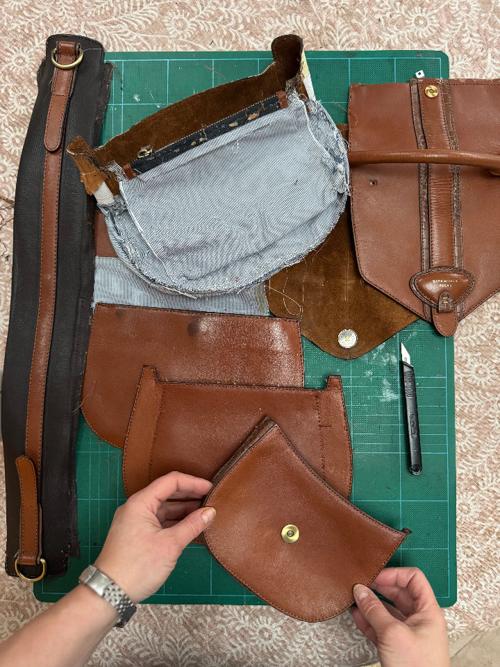 Brown leather bag being assembled on a green cutting mat with tools.