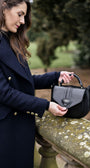 Woman in a navy coat holding a black handbag outdoors.