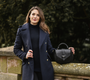 Woman in a dark navy coat holding a black handbag against a blurred natural background