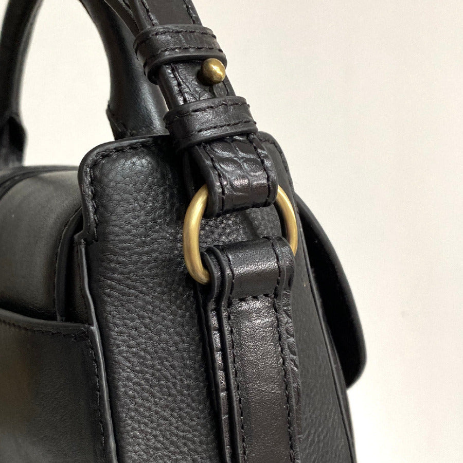 Close-up of a black leather handbag with gold hardware on a light beige background