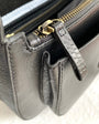 Close-up of a black leather handbag with gold zipper and handle on a light background