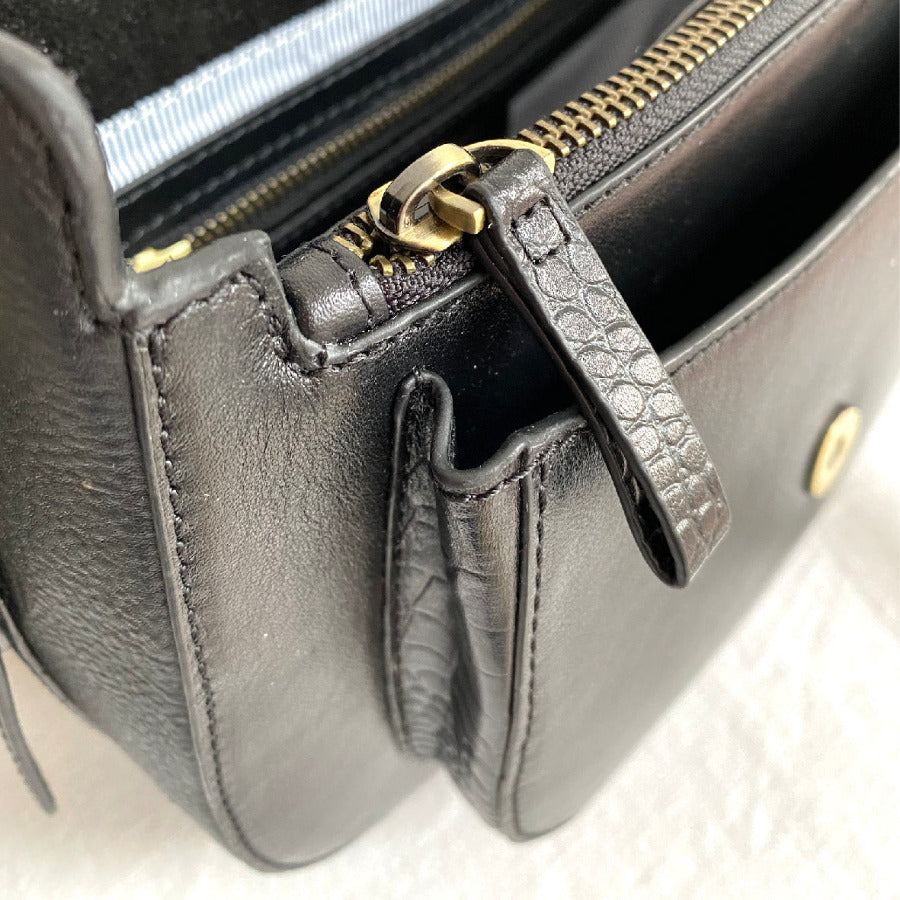 Close-up of a black leather handbag with gold zipper and handle on a light background