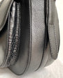 Close-up of a black leather handbag with textured side panel on a light background