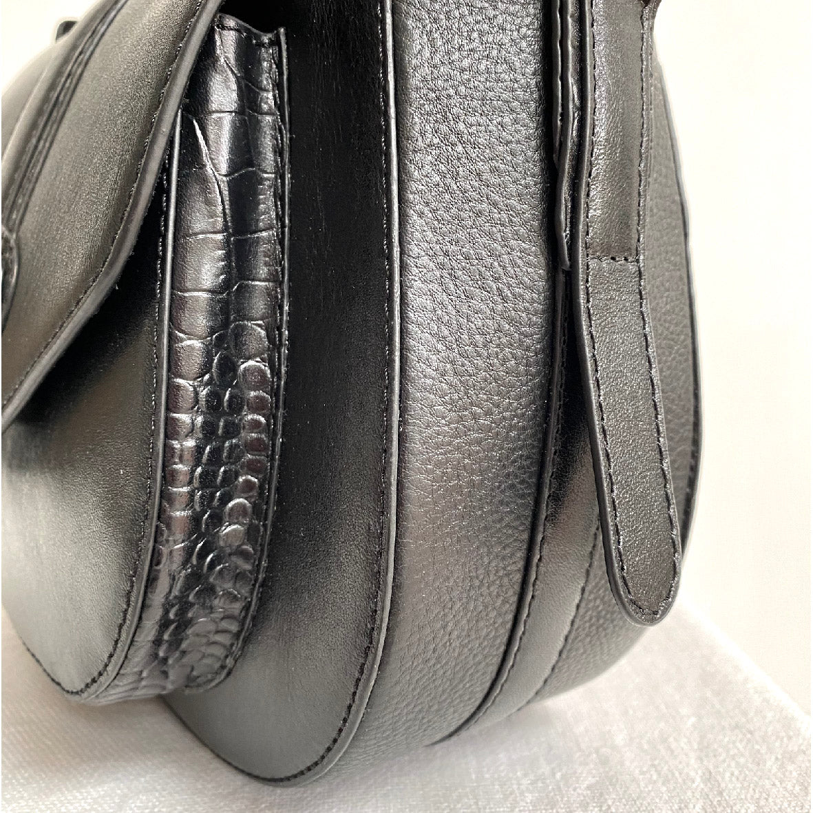 Close-up of a black leather handbag with textured side panel on a light background