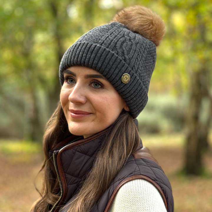 grey cable kit bobble hat with pom worn by pretty girl in a sprig woodland 