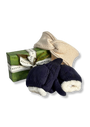 A gift set from Reeve & Barkworth featuring a green wrapped soap bar, a cream knitted hat with a bow, and a pair of navy knit mittens with cream fleece lining, arranged on a white background.
