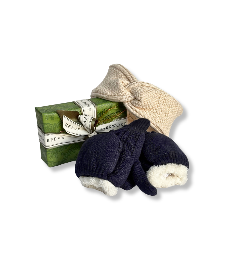 A gift set from Reeve & Barkworth featuring a green wrapped soap bar, a cream knitted hat with a bow, and a pair of navy knit mittens with cream fleece lining, arranged on a white background.