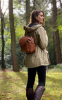 woman in wood in sunshine holding leather rucksack