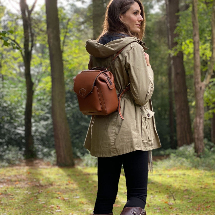 woman in wood in sunshine holding leather rucksack