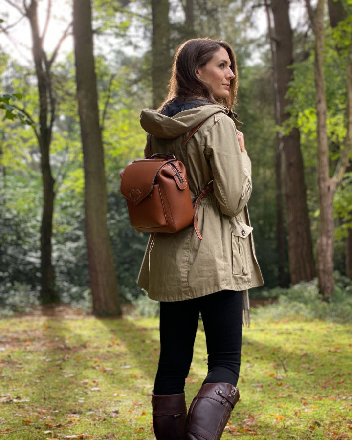 woman in wood in sunshine holding leather rucksack
