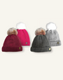 raspberry pink bobble hat with white faux fur pom pom, dark red bobble hat with natural coloured pom, light grey bobble hat with white pom, and dark grey hat with natural coloured pom, all knitted in a mixed cable knit pattern with branded barkworth reeve tab