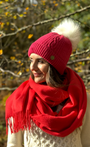 lady wearing raspberry pink bobble hat with white faux fur pom pom and a red scarf , in a autumn wood.