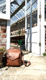 Brown leather bag on a stone floor with a glasshouse and brick wall in the background